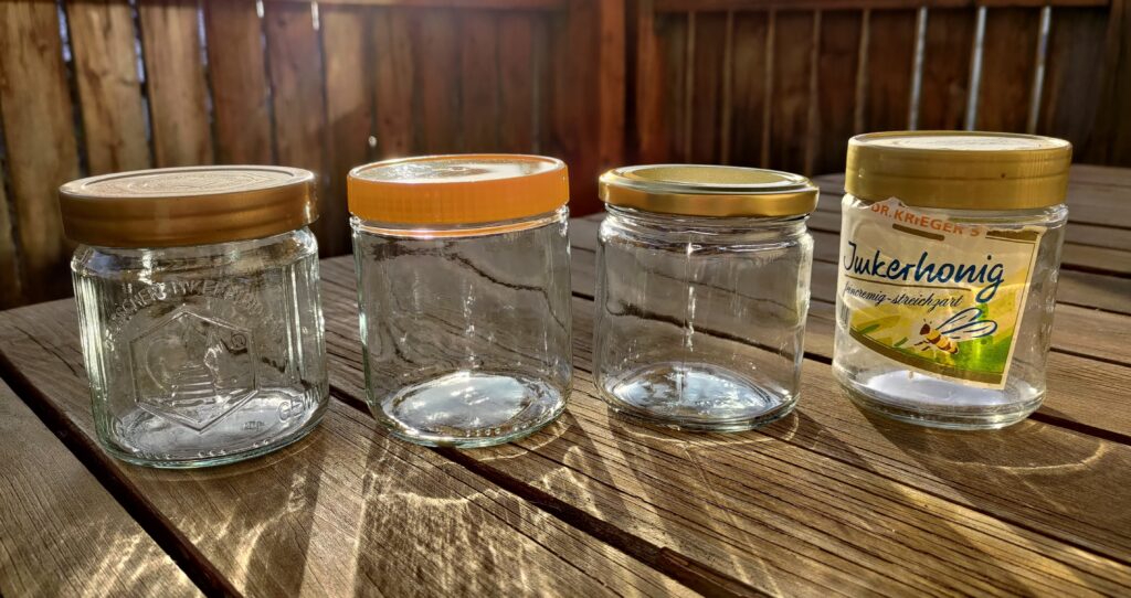 Vier leere Honiggläser stehen nebeneinander auf einem Holztisch.