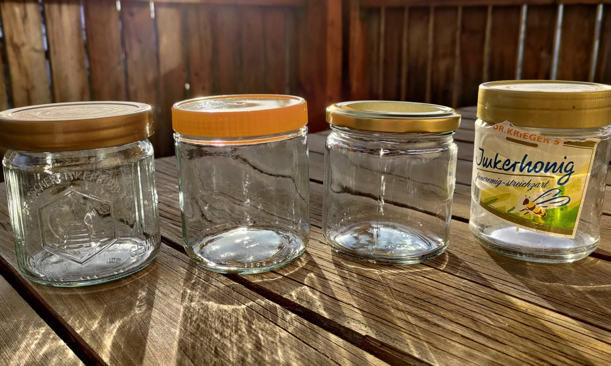 Vier leere Honiggläser stehen nebeneinander auf einem Holztisch.